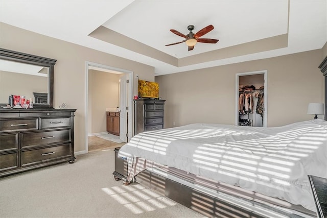 carpeted bedroom with ensuite bath, a raised ceiling, a walk in closet, and ceiling fan