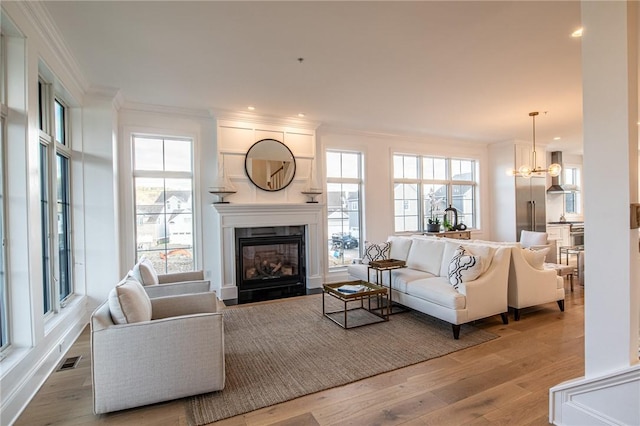 living area featuring a wealth of natural light, ornamental molding, light wood-type flooring, and visible vents