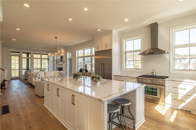 kitchen with premium appliances, white cabinetry, decorative backsplash, wall chimney exhaust hood, and light wood finished floors