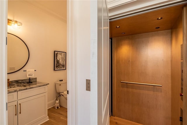 bathroom with baseboards, toilet, elevator, wood finished floors, and vanity