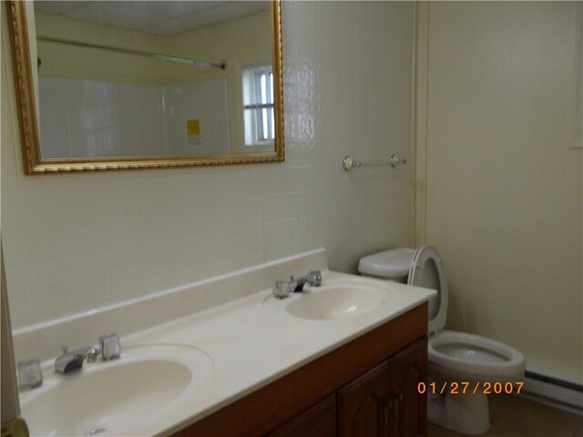 bathroom with dual vanity, toilet, and a baseboard heating unit