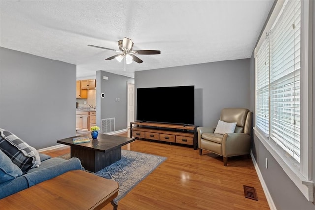 living room with ceiling fan, a textured ceiling, and light hardwood / wood-style floors