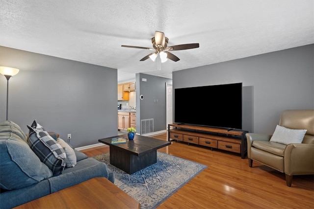 living room with ceiling fan, sink, light wood-type flooring, and a textured ceiling