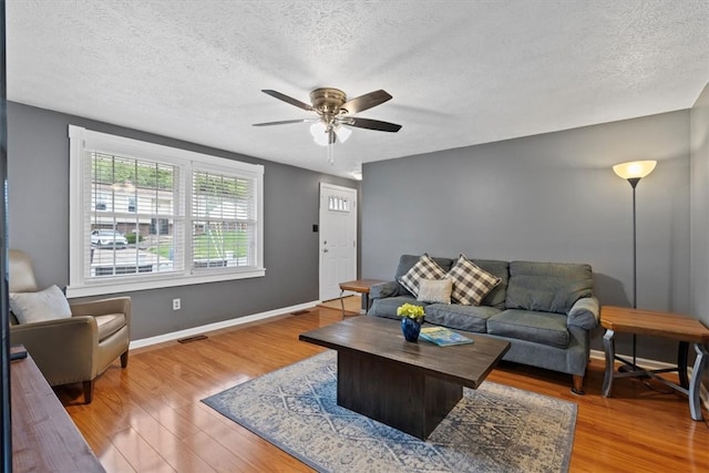 living room with ceiling fan, light wood-type flooring, and a textured ceiling