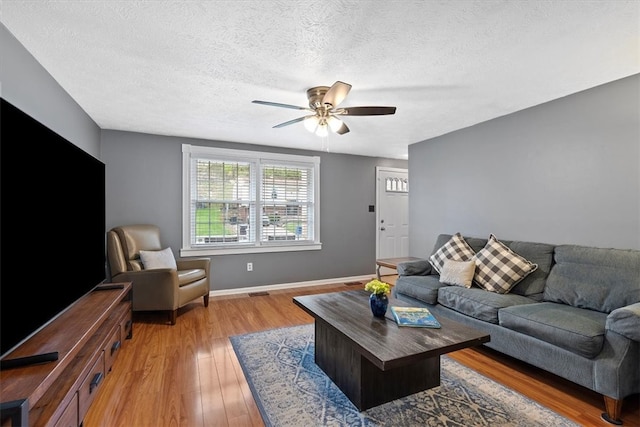 living room with light hardwood / wood-style flooring, a textured ceiling, and ceiling fan