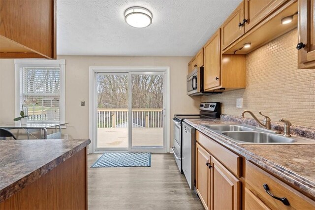 kitchen with a textured ceiling, decorative backsplash, appliances with stainless steel finishes, sink, and light hardwood / wood-style flooring