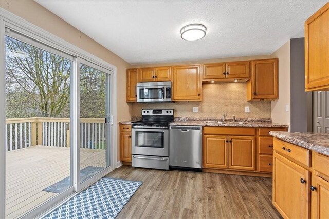 kitchen featuring tasteful backsplash, light wood-type flooring, appliances with stainless steel finishes, light stone countertops, and sink