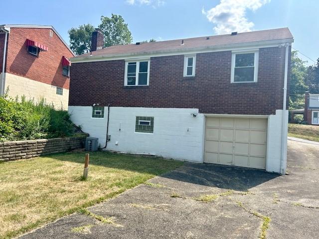 back of property with a garage, a yard, and central AC