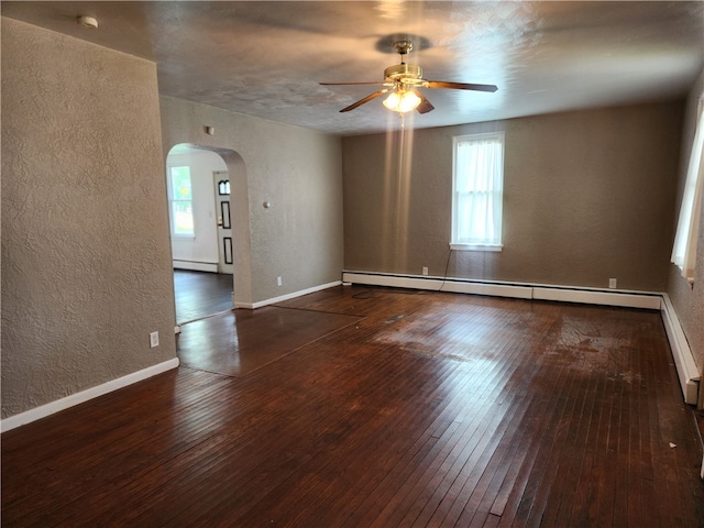 spare room featuring a baseboard heating unit, plenty of natural light, ceiling fan, and dark hardwood / wood-style floors