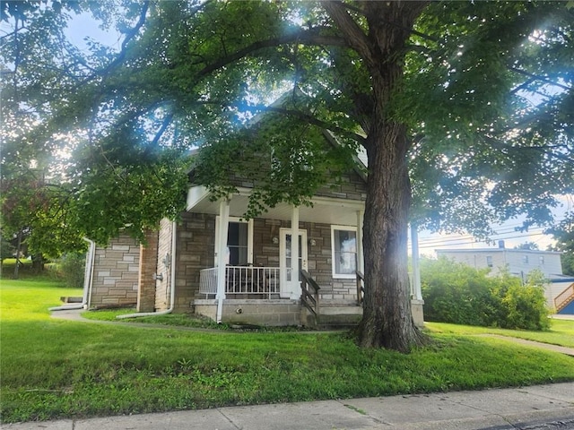 view of property hidden behind natural elements with a porch, stone siding, and a front lawn