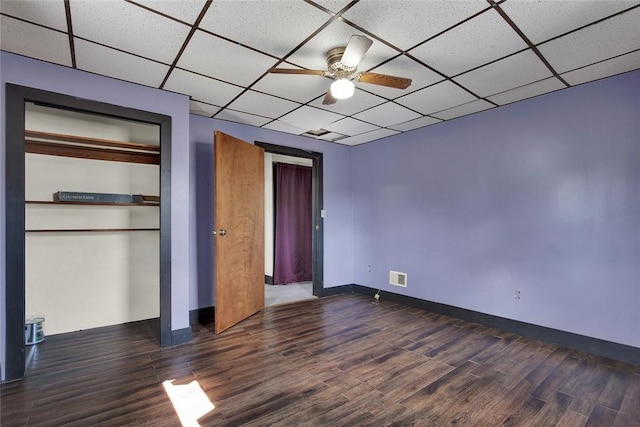 unfurnished bedroom with a paneled ceiling, dark wood-style flooring, visible vents, baseboards, and a closet