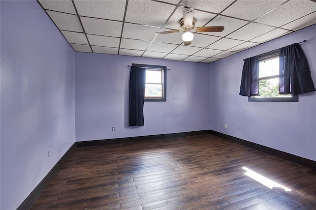 empty room with dark wood-type flooring, baseboards, a drop ceiling, and a wealth of natural light