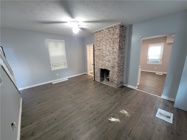 unfurnished living room with dark wood-type flooring, a textured ceiling, ceiling fan, a fireplace, and brick wall