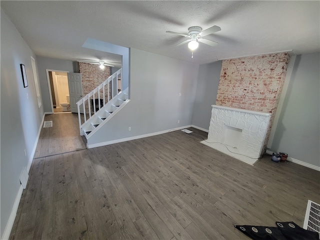 unfurnished living room featuring ceiling fan, a textured ceiling, brick wall, and hardwood / wood-style flooring