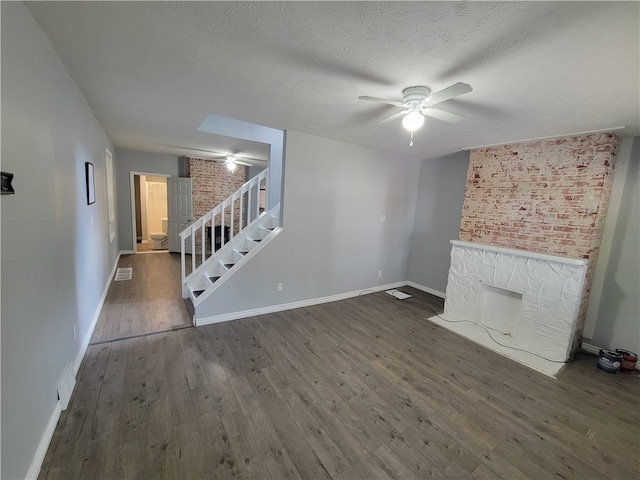 unfurnished living room with ceiling fan, wood-type flooring, a textured ceiling, and brick wall