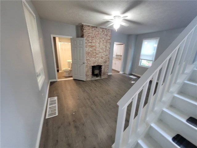 living room with a textured ceiling, hardwood / wood-style floors, ceiling fan, a fireplace, and brick wall