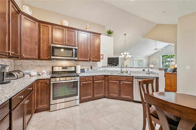 kitchen featuring ceiling fan with notable chandelier, appliances with stainless steel finishes, light tile patterned floors, vaulted ceiling, and sink