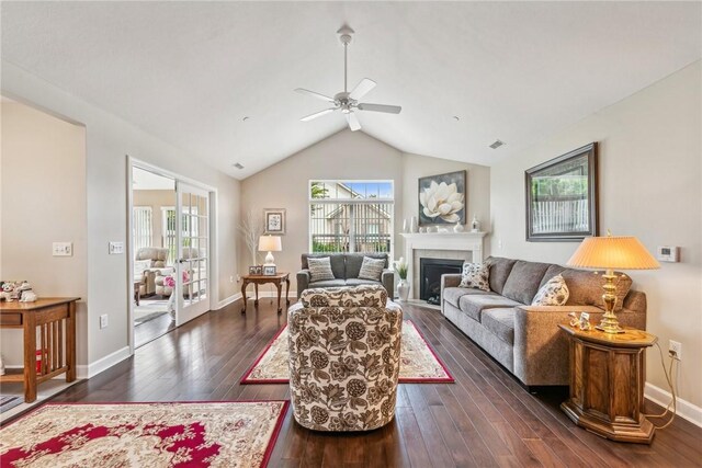 living room with ceiling fan, dark wood-type flooring, a tiled fireplace, and vaulted ceiling