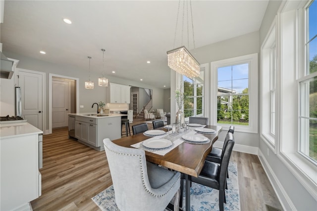 dining room with light wood-type flooring, sink, an inviting chandelier, and a healthy amount of sunlight