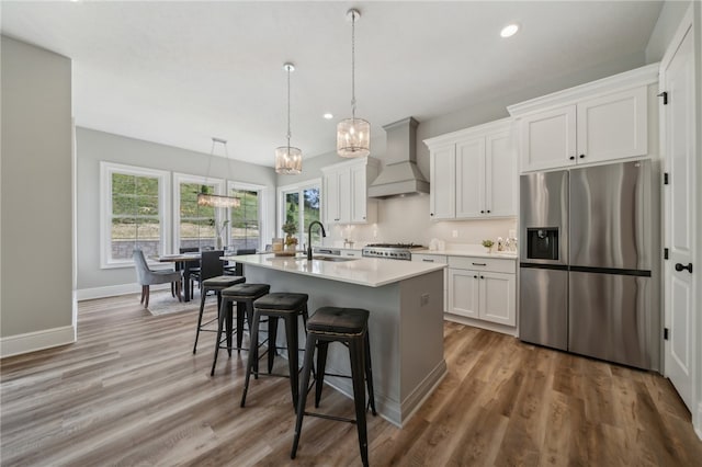 kitchen featuring hardwood / wood-style flooring, white cabinetry, premium range hood, and stainless steel refrigerator with ice dispenser