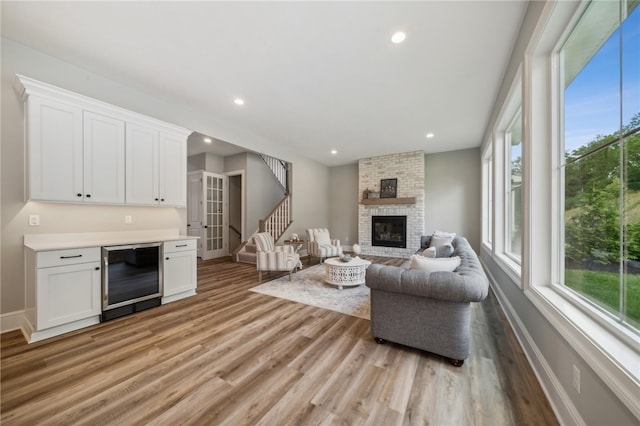 living room featuring wine cooler, plenty of natural light, light hardwood / wood-style flooring, and a brick fireplace