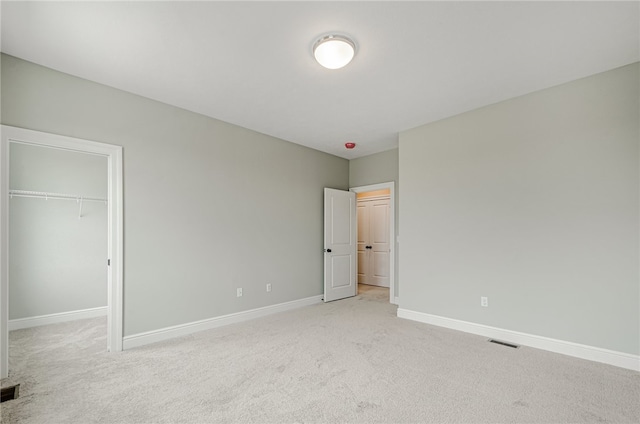 unfurnished bedroom with light colored carpet, a closet, and a spacious closet