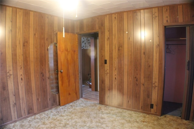 unfurnished bedroom featuring light colored carpet, a closet, and wood walls