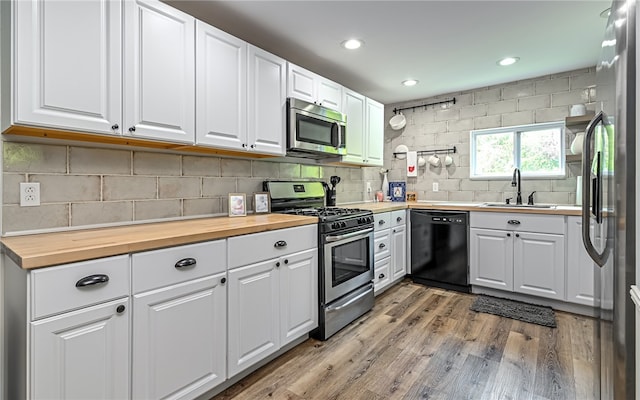 kitchen featuring stainless steel appliances, decorative backsplash, wood-type flooring, and white cabinets