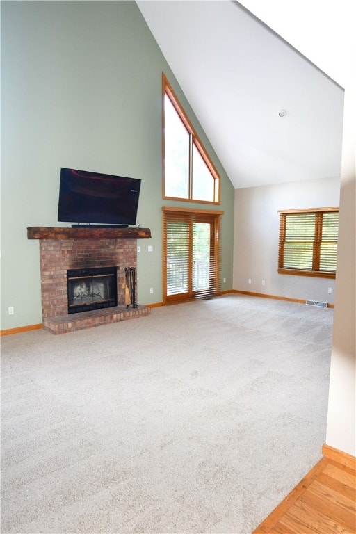 unfurnished living room featuring light carpet, high vaulted ceiling, and a brick fireplace