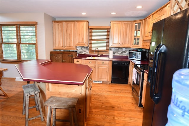 kitchen featuring light wood-type flooring, tasteful backsplash, light brown cabinetry, sink, and black appliances