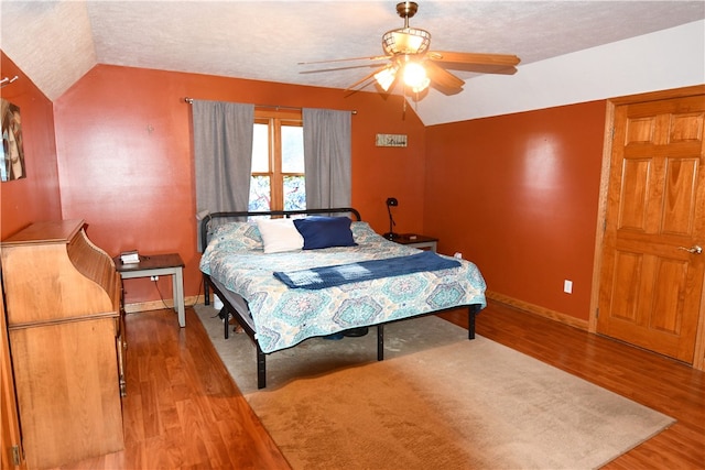 bedroom with ceiling fan, vaulted ceiling, hardwood / wood-style floors, and a textured ceiling