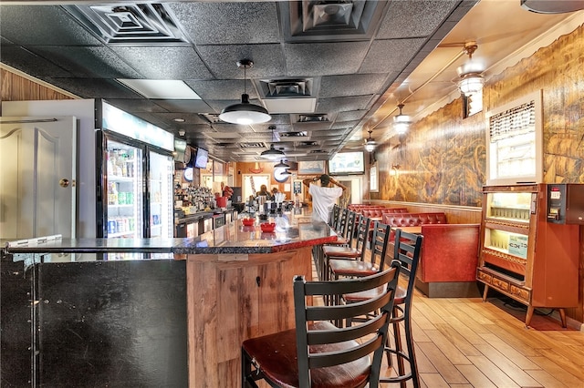 bar with light wood-type flooring, decorative light fixtures, and a paneled ceiling