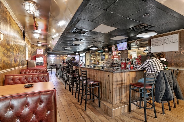 bar with hardwood / wood-style flooring, wood walls, and a drop ceiling