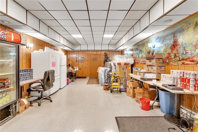 basement featuring tile patterned floors, wood walls, white refrigerator, and a paneled ceiling