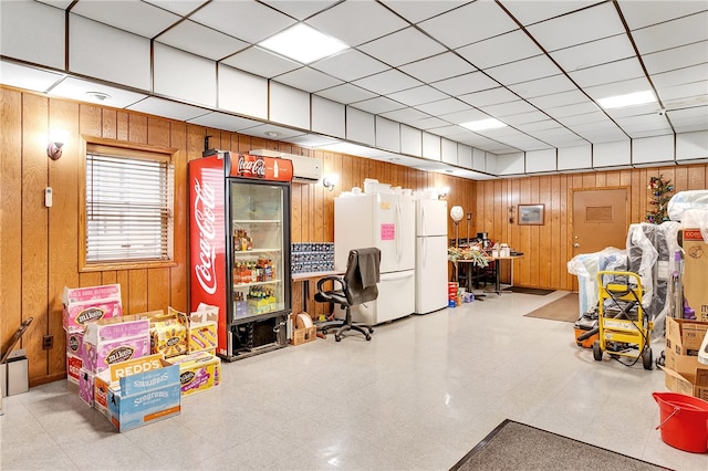 basement with a drop ceiling, wooden walls, and white fridge