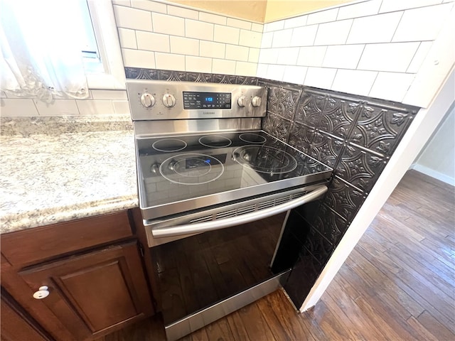 details with backsplash, stainless steel electric stove, dark hardwood / wood-style flooring, and light stone counters