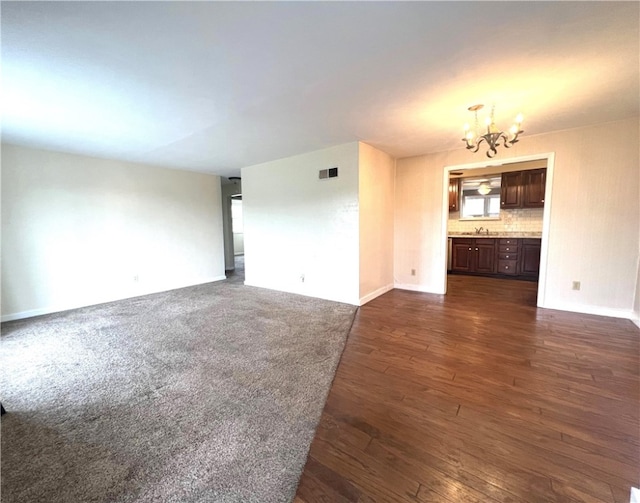 unfurnished living room featuring sink, dark wood-type flooring, and a notable chandelier