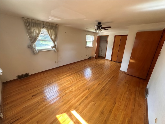 unfurnished bedroom featuring multiple closets, multiple windows, ceiling fan, and light hardwood / wood-style flooring