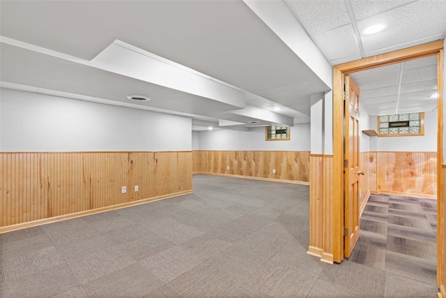 basement featuring a drop ceiling, carpet, and wood walls