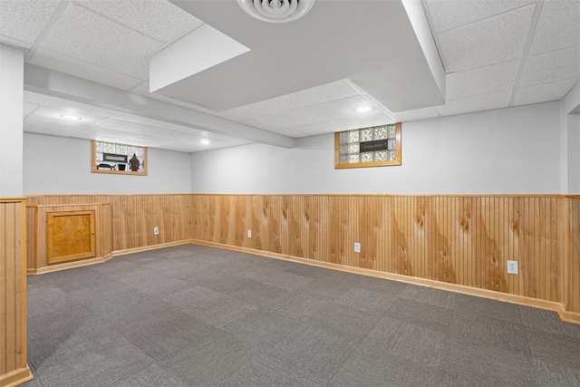 basement with dark carpet, a paneled ceiling, and wooden walls