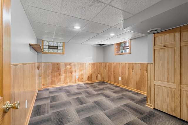 basement with dark colored carpet, a healthy amount of sunlight, and wood walls