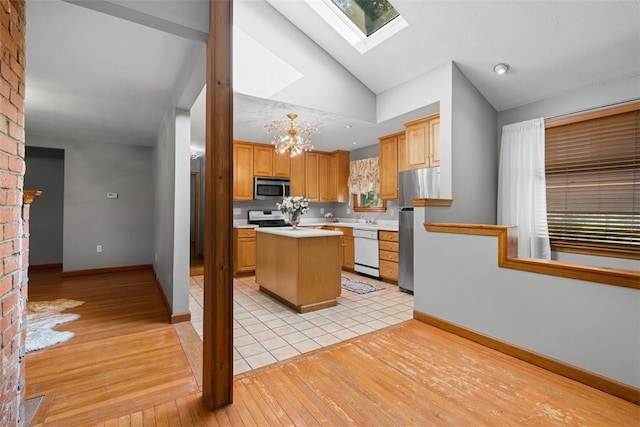 kitchen with pendant lighting, appliances with stainless steel finishes, a center island, vaulted ceiling with skylight, and light hardwood / wood-style floors