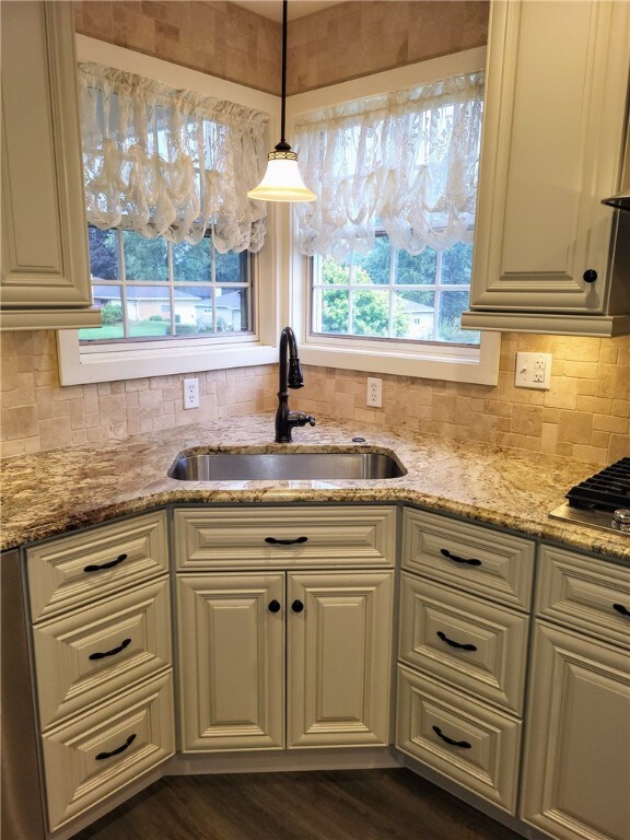 kitchen featuring sink, dark hardwood / wood-style flooring, decorative backsplash, light stone counters, and pendant lighting