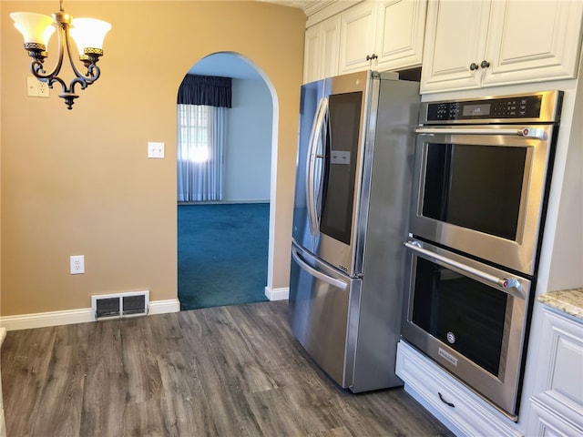 kitchen with an inviting chandelier, appliances with stainless steel finishes, light stone counters, dark carpet, and white cabinetry