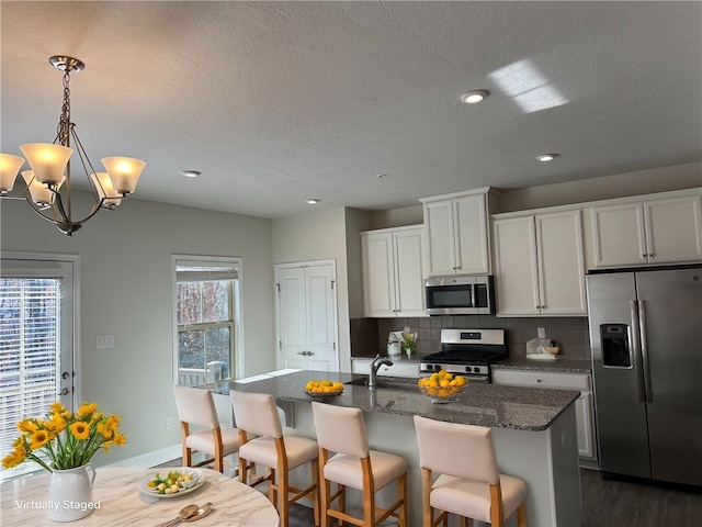 kitchen featuring stainless steel appliances, a center island with sink, dark hardwood / wood-style floors, backsplash, and dark stone countertops