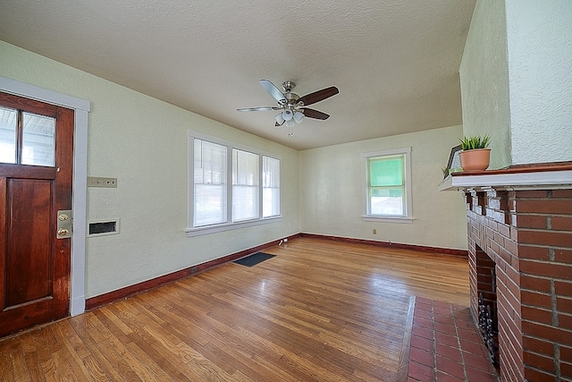 unfurnished living room featuring a textured ceiling, ceiling fan, hardwood / wood-style floors, and a brick fireplace