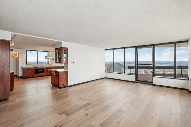 unfurnished living room featuring a notable chandelier, a textured ceiling, light wood-type flooring, and a wealth of natural light