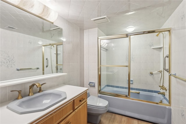 full bathroom featuring hardwood / wood-style flooring, toilet, vanity, tile walls, and enclosed tub / shower combo