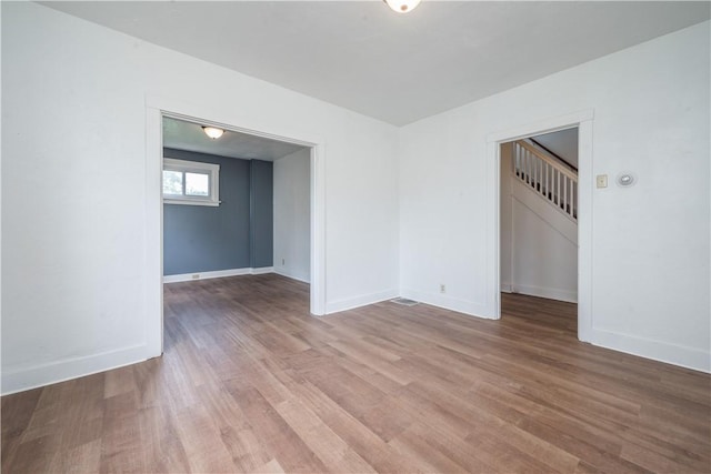 empty room with stairway, light wood-type flooring, and baseboards