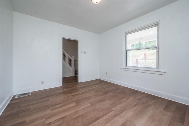 spare room with visible vents, stairway, baseboards, and wood finished floors